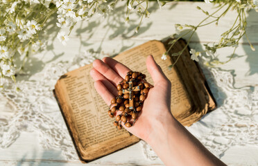 Hands folded in prayer over old Holy Bible. Wooden background.Hands and rosary, prayer, old book with yellow pages. white flowers on a background. in the garden. Concept of prayer and religion
