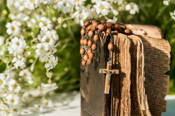 Hands folded in prayer over old Holy Bible. Wooden background.Hands and rosary, prayer, old book with yellow pages. white flowers on a background. in the garden. Concept of prayer and religion