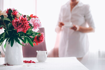 Woman having cup of coffee in the kitchen decorated with pink peonies.