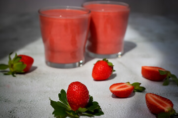 Organic strawberry smoothies in glass cups and berries of ripe strawberries on a gray cement background.