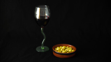 

Glass of red wine and green olives, aperitif, on black background