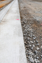 Long view down freshly extruded concrete curb beside road bed under construction, vertical aspect