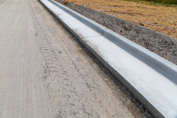 New road under construction, dirt roadway edged with freshly formed concrete curbing, copy space, horizontal aspect