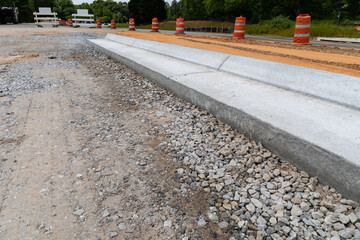 Traffic barricades alongside a new street under construction, gravel road bed with extruded concrete curb, horizontal aspect