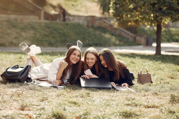 Students in a park. Girls lying on a grass. Friends with a laptop.