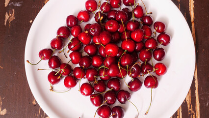 Top view of a lot of fresh sweet cherry fruit berries with water drops. Close-up on the plate on wooden background.  Large collection of fresh red cherries. Ripe cherries texture