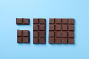Tasty milk chocolate on light blue background, flat lay