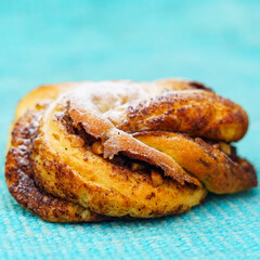 Close-up view of sweet cinnamon roll on the blurred turquoise background. Danish pastry. Sweet pastry for breakfast or snack.