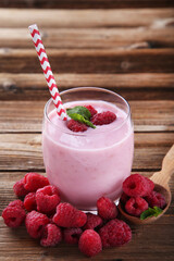 Raspberry smoothie in glass with straw on brown wooden table