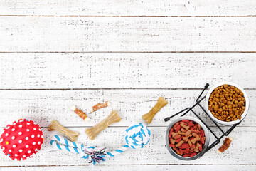 Dry pet food in bowls with toys on white wooden table
