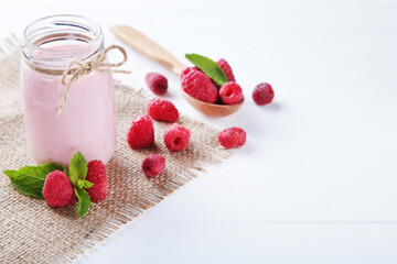 Raspberry smoothie in glass jar with spoon on white wooden table