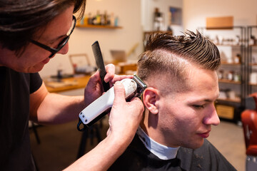 Barber trims the hair of young man with a razor