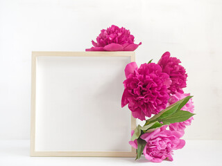 Flower composition. Layout with empty wooden photo frame and lush red and pink peonies. Drops of water are on the petals. Light background. Copy space.