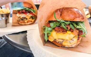 Two burgers with juicy cutlet, fresh vegetables, arugula, cheese and bacon in a crispy bun in kraft packaging. Delicious traditional fast food and street food - grilled burgers. Junk food to eat.