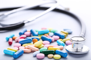Colorful pills with stethoscope on grey background