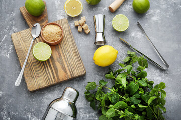 Barman equipments with limes, lemons and mint leafs on grey wooden table