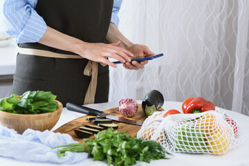 women's hands with smartphone in kitchen, cooking vegetables, cooking at home