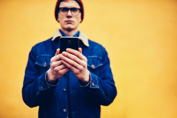 Selective focus on modern smartphone device connected to 4G internet in blogger's hands.Blurred background with hipster guy holding cellular and chatting online in social networks standing outdoors