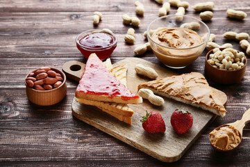 Bread with peanut butter, jam, fruits and nuts on brown wooden table