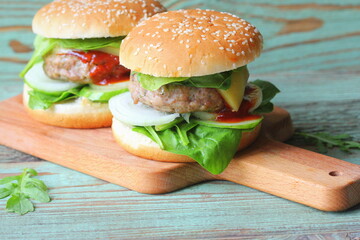 Homemade hamburger with beef, onion,cucumber, lettuce, cheese, spinach and spices. Fresh burger closeup on wooden cutting board