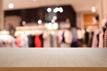 Empty wooden table and blurred view of store with modern clothes