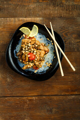 Nastol black plate with funchose and chicken with vegetables in pad Thai sauce next to chopsticks.