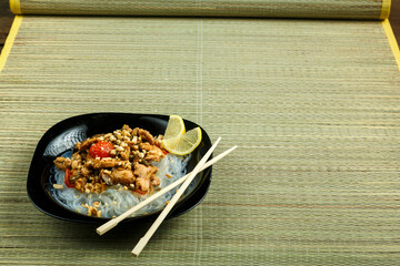 plate with funchose and chicken with vegetables in pad Thai sauce next to chopsticks on a bamboo mat.