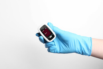Doctor in gloves holding fingertip pulse oximeter on white background, closeup