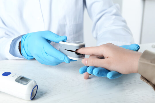Doctor examining patient with fingertip pulse oximeter at white wooden table, closeup