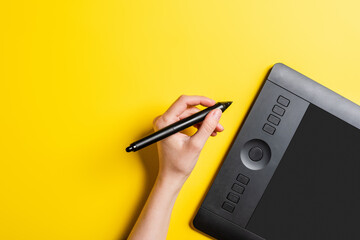 cropped view of designer holding stylus near drawing tablet with blank screen on yellow