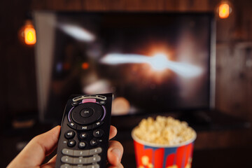 Man with TV remote control sitting at home with a big bowl of popcorn