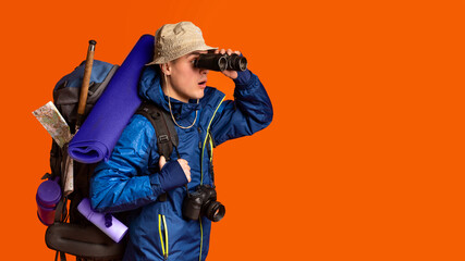 Backpacker using binoculars, looking at free space over orange background