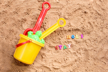 Fototapeta na wymiar Beach sand with toys for the baby, water, the word holi saty in colored letters.