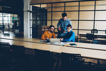 Experienced coach of working team checking project on laptop discussing ideas together, group of IT...