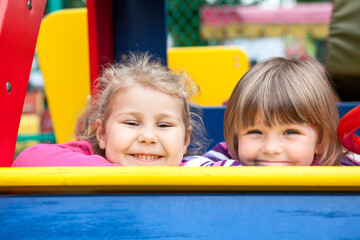 Fototapeta na wymiar Two cheerful little girls laughing while sitting in frame of children playground, foxlike behaviour