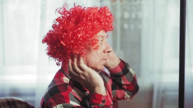 A man in front of a mirror puts on a clown wig with white curls.