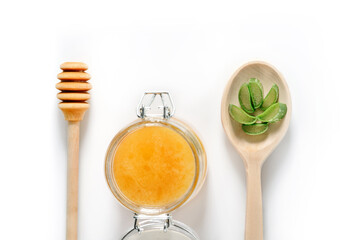 Jar of honey, a wooden spoon for honey and a spoon with chopped aloe vera leaves.