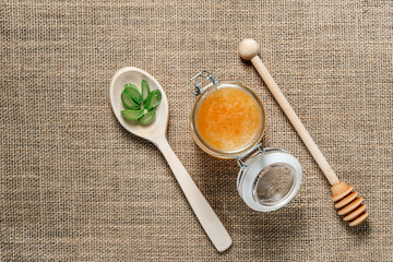 Jar of honey, a wooden spoon for honey and a spoon with chopped aloe vera leaves on burlap.