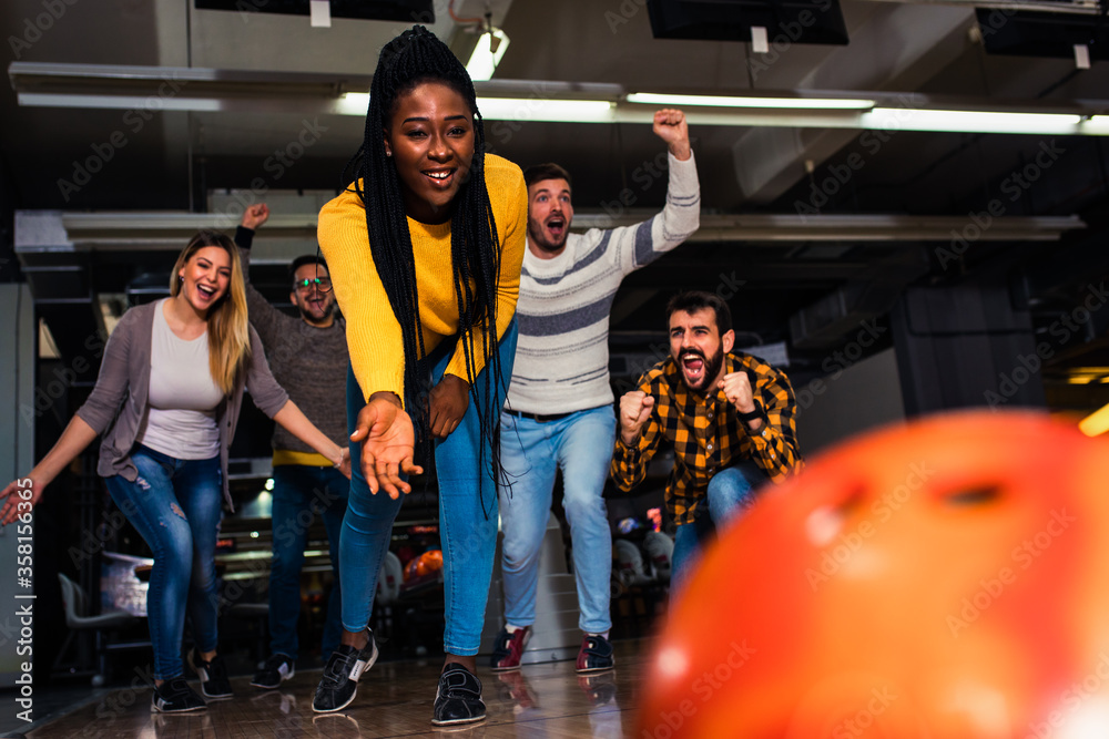 Wall mural Group of friends enjoying time together laughing and cheering while bowling at club.