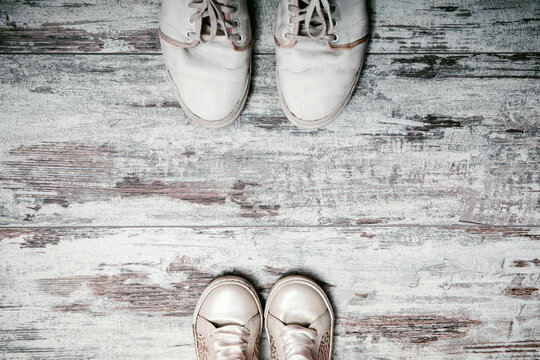 Conceptual image of gumshoes sneakers of father and baby son daughter on white shabby chic wooden background. With copy space in single parent family. Fathers day, Parenting and lifestyle concept.
