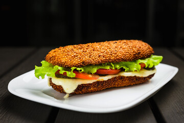 A sandwich with hot mozzarella, tomato, lettuce and pickles on a sesame bun