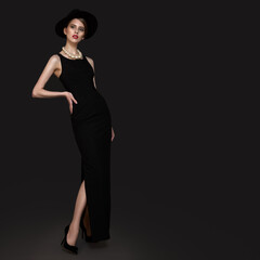 Fototapeta premium Woman in a black long dress necklace and hat. Beautiful pose. Part of the leg. photo in full growth. copycpase