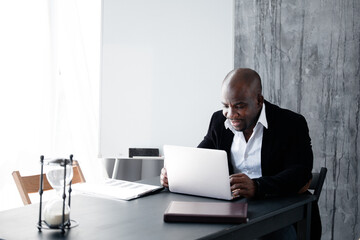 Dark-skinned fellow in a business suit working at a laptop in the office. The employee is African...