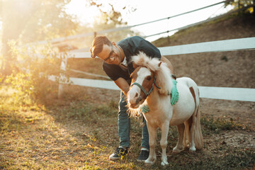 Young attractive male veterinarian enjoying with adorable little pony horse.
