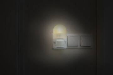 Night light plug in white socket on white wall turns on automatically in modern house by night in the dark