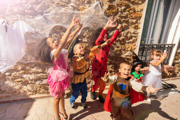 Group of kids lift hands in the air reaching for candies wearing Halloween costumes standing by the wall with ghost on it