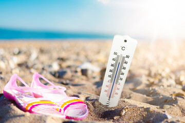 summer weather and hear concept, thermometer in sand at beach against sea and blue sky