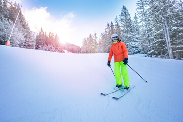 Confident teenager in orange yellow outfit mountain ski portrait on the slope between snow covered firs