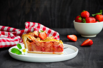 Pie with rhubarb and strawberries on a dark wooden background with fresh strawberries. Horizontal orientation.