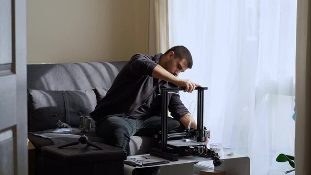 Man assambling 3d printer in front of smartphone at home